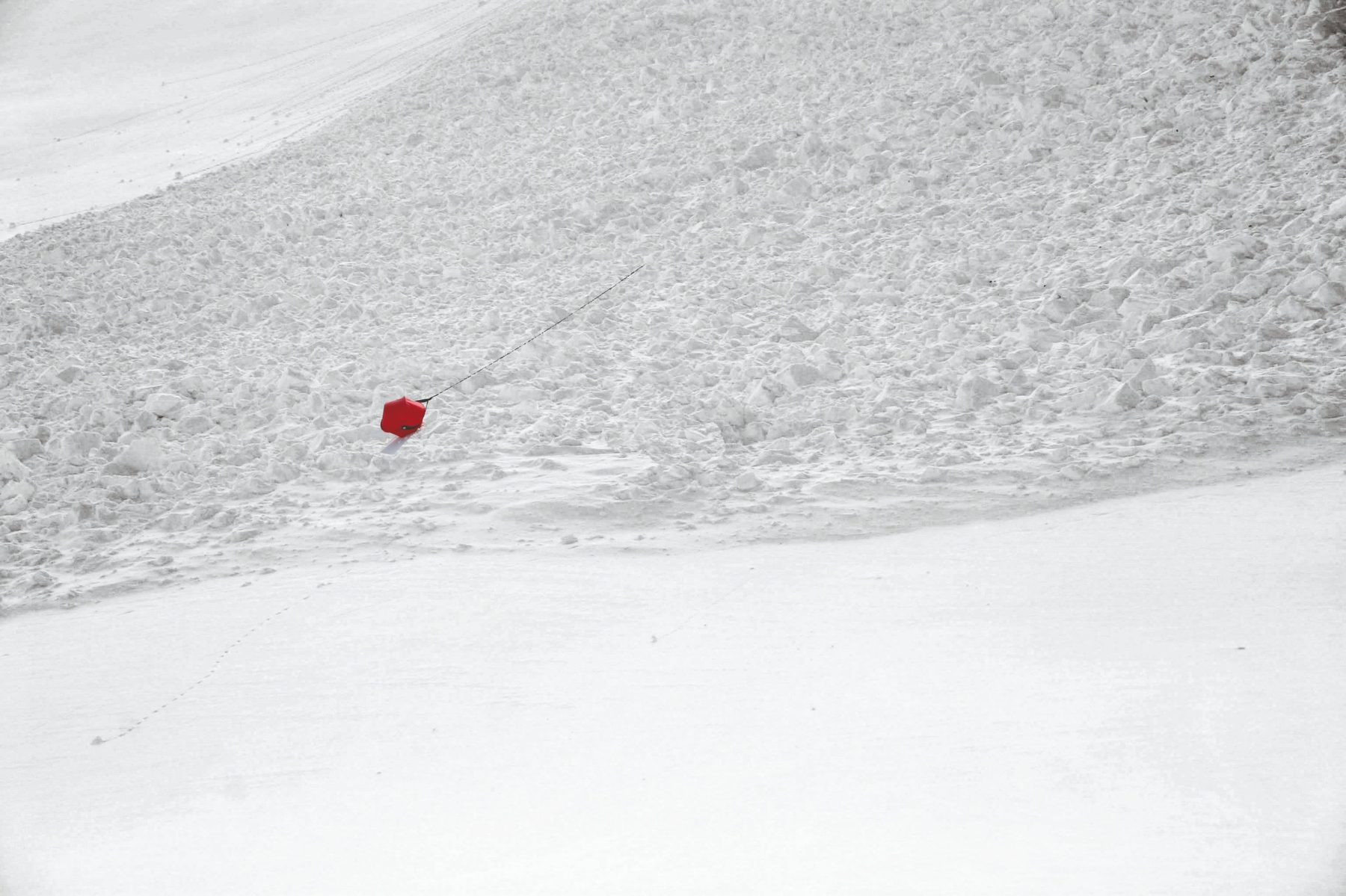 Roter Avalanche Ball liegt auf einem Lawinenkegel, die Leine führt in den Schnee