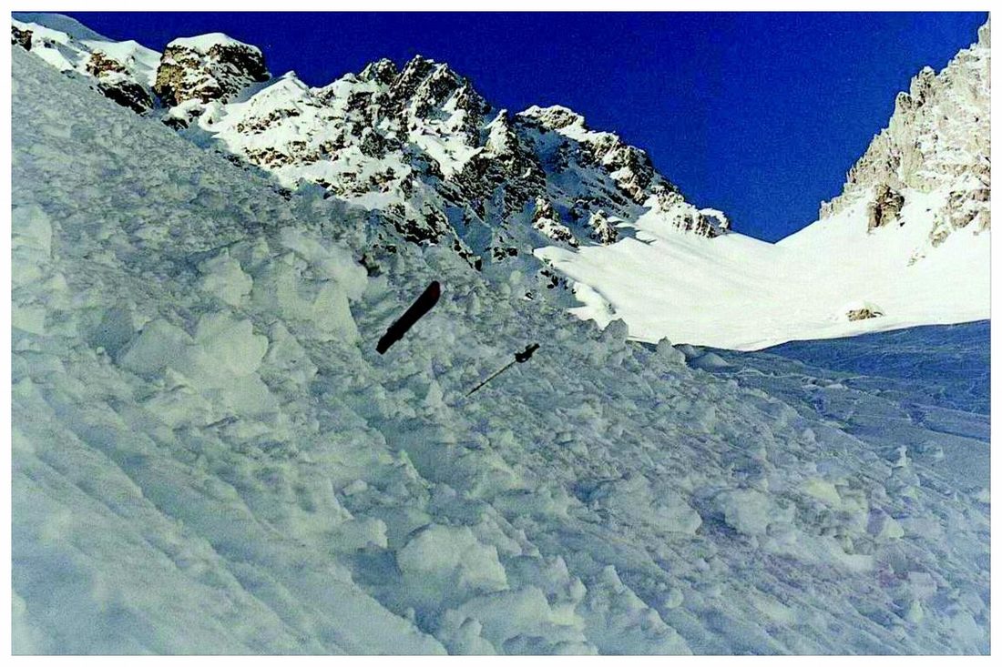 Lawinenkegel unter einem Felsgrat, sichtbar ragen ein Ski und ein Stock heraus